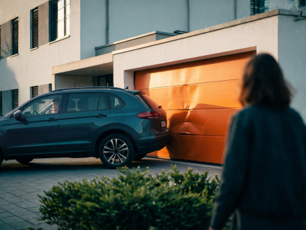 Frau betrachtet ein beschädigtes Auto vor einer Garage