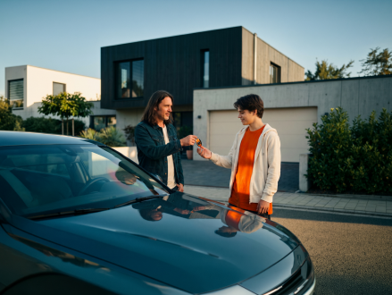 Übergabe eines Autoschlüssels zwischen zwei Personen neben einem Auto