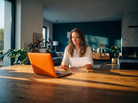 Frau prüft eine Rechnung und Unterlagen an ihrem Laptop