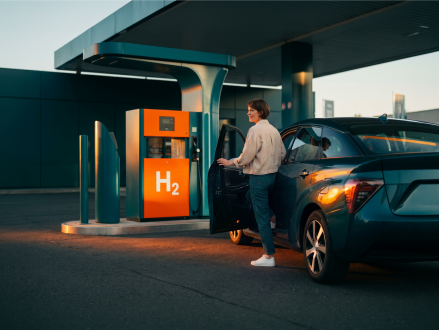 Frau betankt ein Auto an einer Wasserstofftankstelle