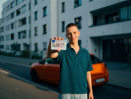 Junger Autofahrer zeigt seinen Führerschein vor einem Auto