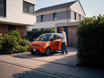 Junger Mann steht neben einem kompakten Microcar vor einem Wohnhaus