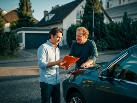 Zwei Männer besprechen Fahrzeugunterlagen neben einem Auto