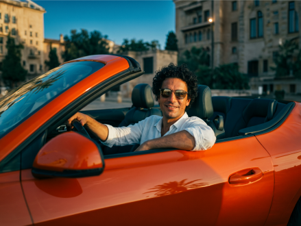 Mann sitzt am Steuer eines orangefarbenen Cabriolets