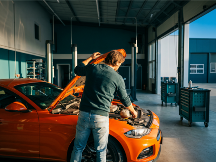 Mechaniker kontrolliert den geöffneten Motorraum eines Autos in der Werkstatt