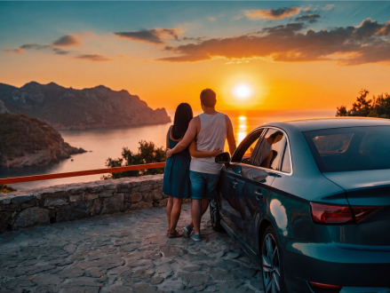 Paar steht neben seinem Auto und blickt bei Sonnenuntergang über die Landschaft