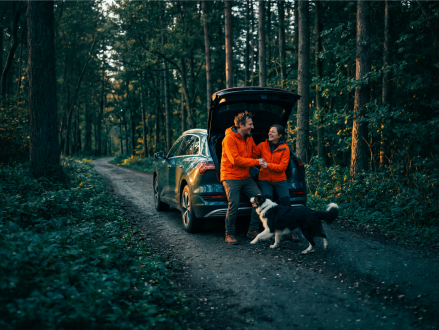 Paar sitzt mit seinem Hund am offenen Kofferraum eines Autos im Wald
