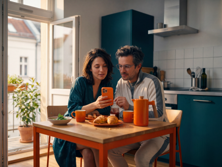 Paar nutzt beim gemeinsamen Frühstück ein Smartphone am Küchentisch