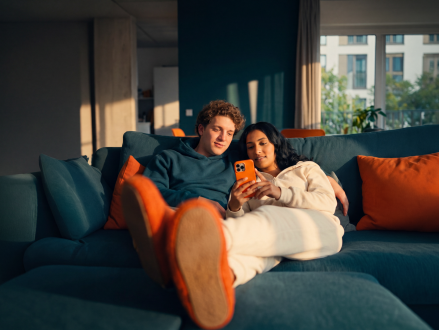 Paar liegt gemeinsam auf dem Sofa und schaut auf ein Smartphone