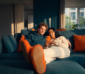 Paar liegt gemeinsam auf dem Sofa und schaut auf ein Smartphone