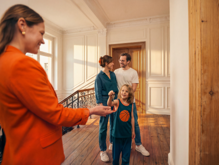 Frau übergibt einer Familie die Schlüssel zu ihrem neuen Zuhause