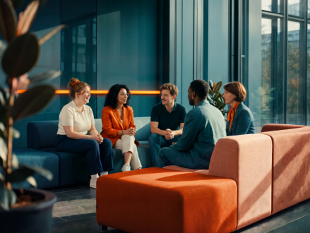 Mitarbeitende sitzen bei einem Teammeeting gemeinsam in einer Bürolounge