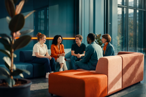 Mitarbeitende sitzen bei einem Teammeeting gemeinsam in einer Bürolounge