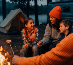 Familie sitzt beim Camping gemeinsam an einem Lagerfeuer
