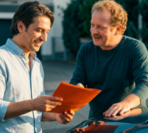 Zwei Männer besprechen Fahrzeugunterlagen neben einem Auto