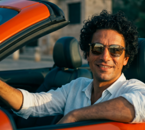 Mann sitzt am Steuer eines orangefarbenen Cabriolets