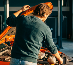 Mechaniker kontrolliert den geöffneten Motorraum eines Autos in der Werkstatt
