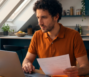 Mann bearbeitet Versicherungsunterlagen und Dokumente am Laptop