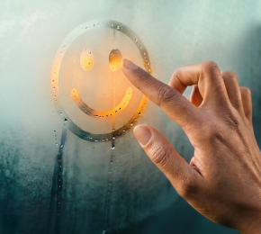 Hand zeichnet einen Smiley auf eine beschlagene Autoscheibe