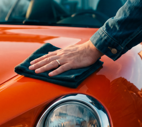Hand poliert die Motorhaube eines orangefarbenen Sportwagens