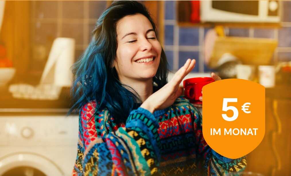 Eine junge Frau sitzt in einer Küche mit einer Tasse in der Hand und unterhält sich.